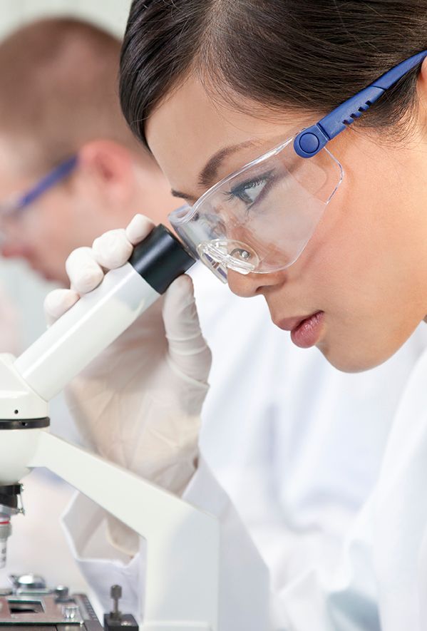 A woman is looking through a microscope in a lab.