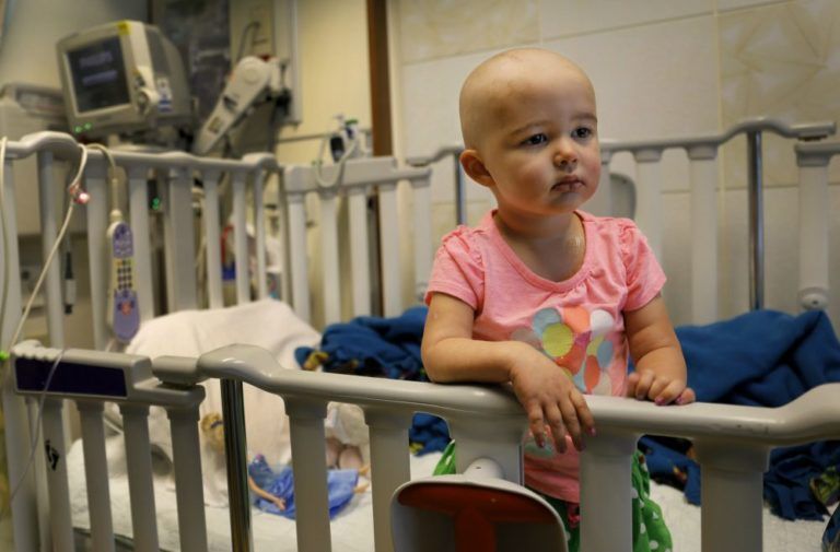 A little girl is sitting in a crib in a hospital room.