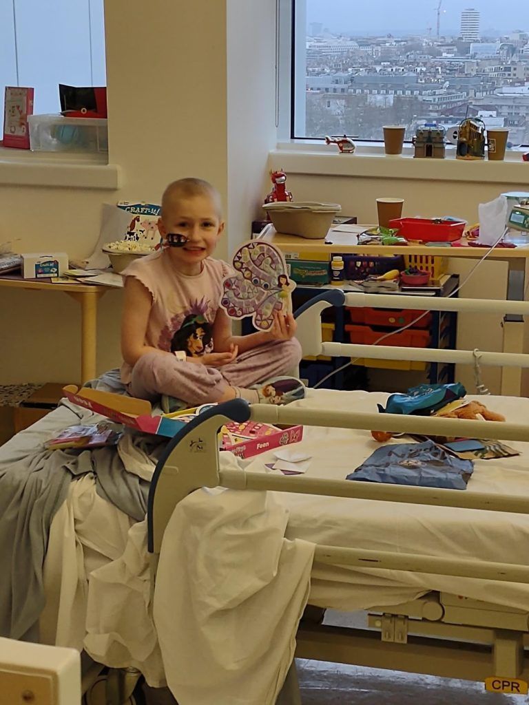 A little girl is sitting on a hospital bed holding a doll