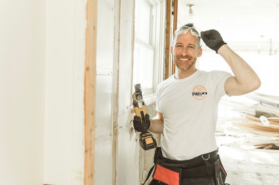 A smiling drywall contractor wearing a white shirt shows off his strength while working with power tools on drywall installation in a bright construction space. This drywall contractor is servicing a job site near Gold Planning Ct, and E Dutchmans Trail, Gold Canyon, AZ.