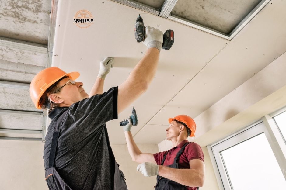 A team of skilled drywall contractors wearing protective hard hats work together to install ceiling drywall panels in a New River construction site. They are working on a project near N 9th Street and Speer Trail in New River, Arizona.