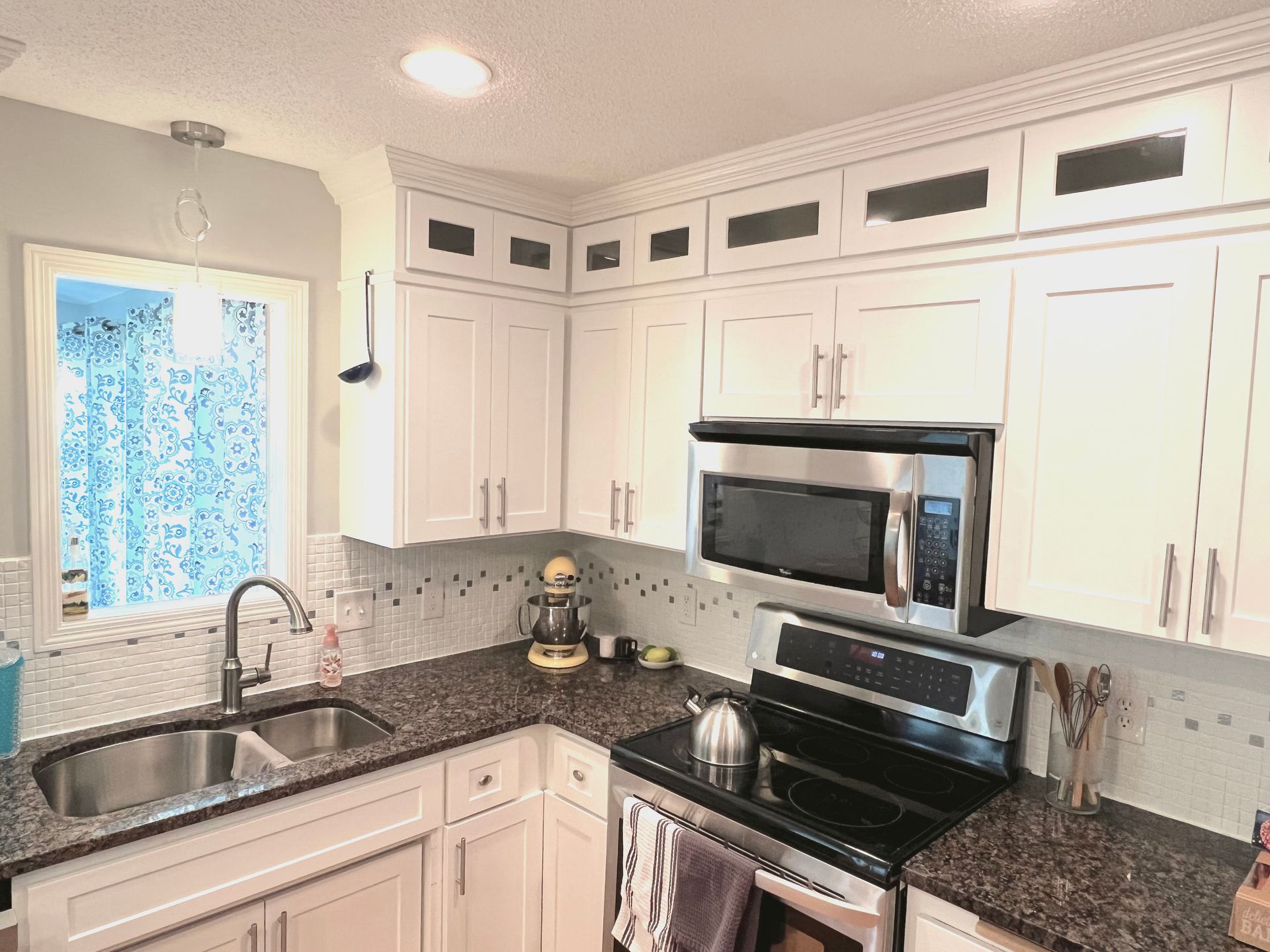A kitchen with white cabinets , stainless steel appliances , granite counter tops and a sink.