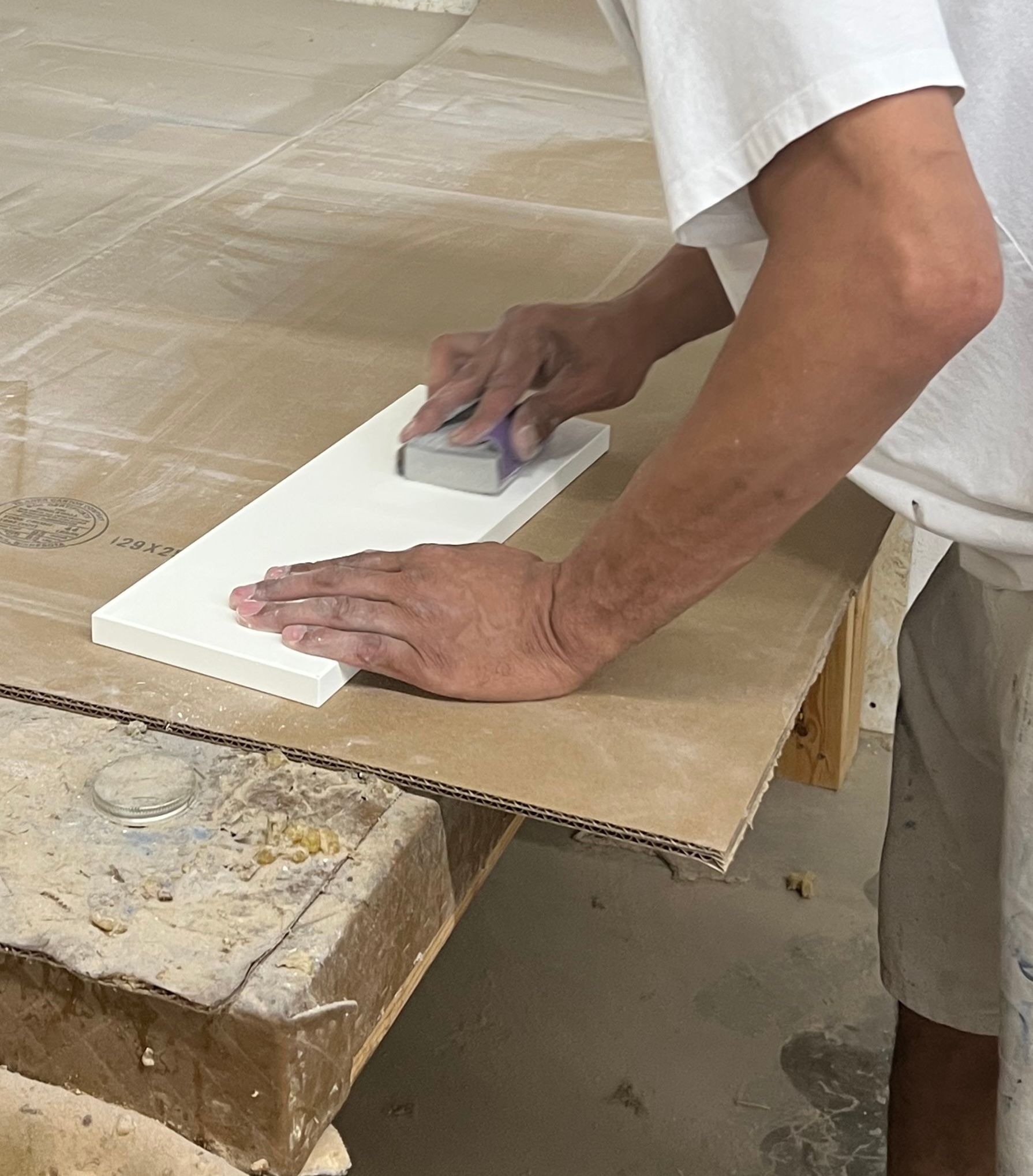 A man is sanding a piece of wood with a sanding block.