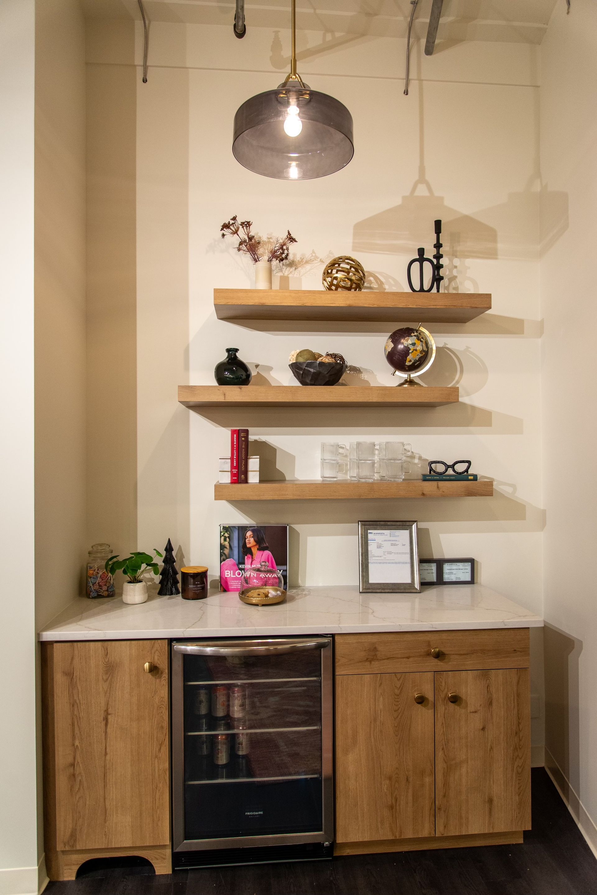 A kitchen with wooden cabinets , shelves , a refrigerator and a pendant light.