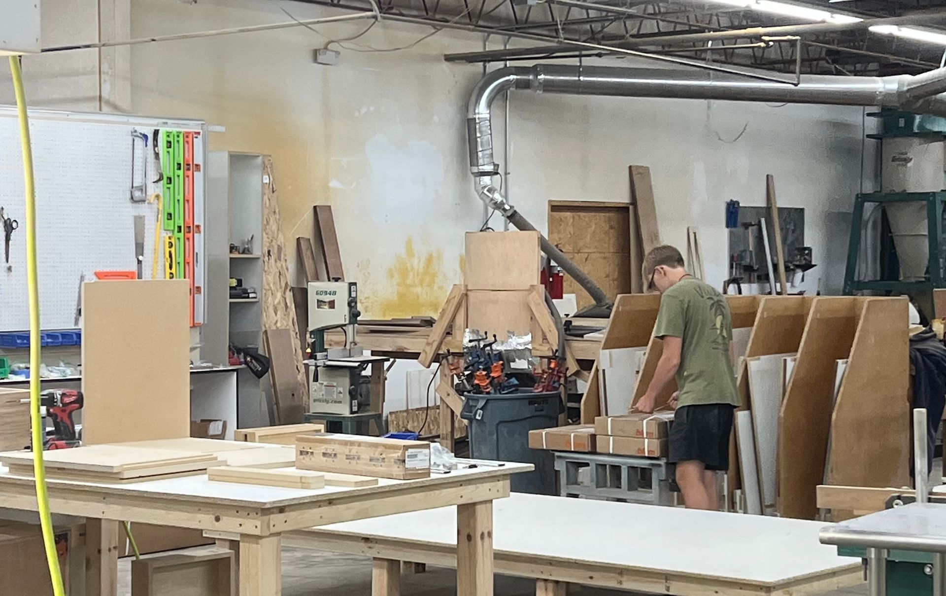 A man in a green shirt is working in a woodworking shop.