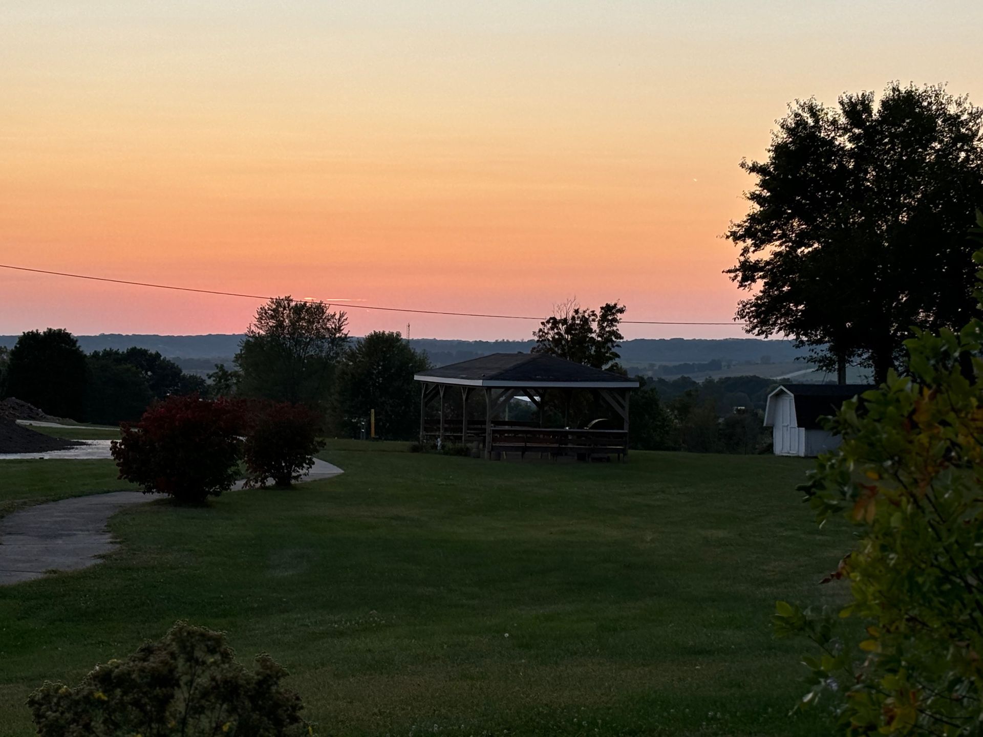 A gazebo in a field with a sunset in the background