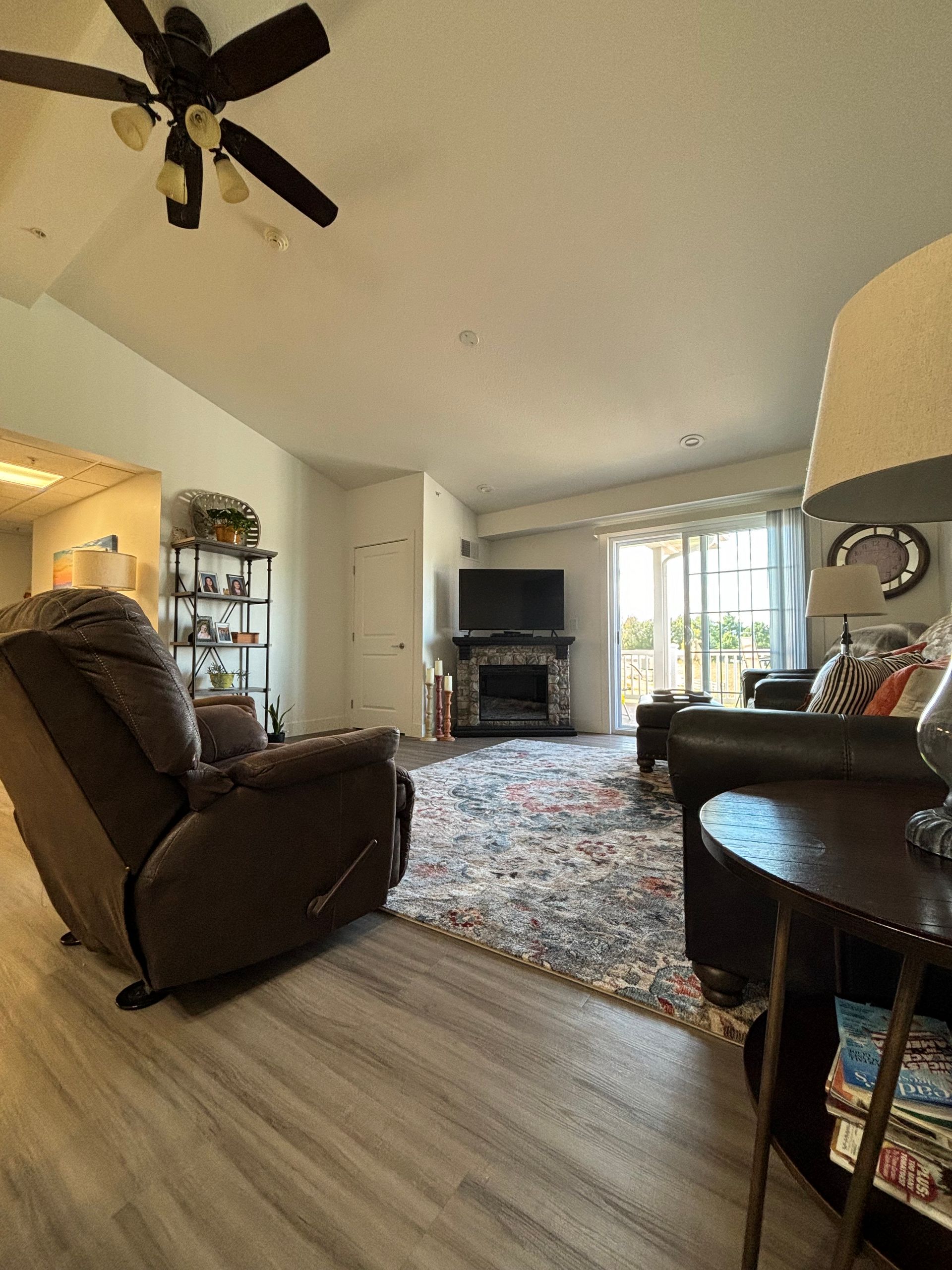 A living room with a ceiling fan , couch , chair , lamp and television.