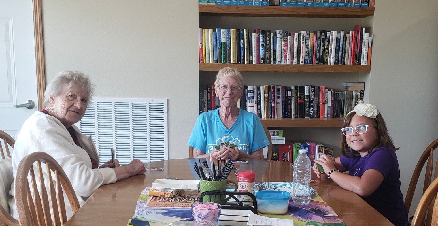 Three people are sitting at a table in front of a bookshelf.