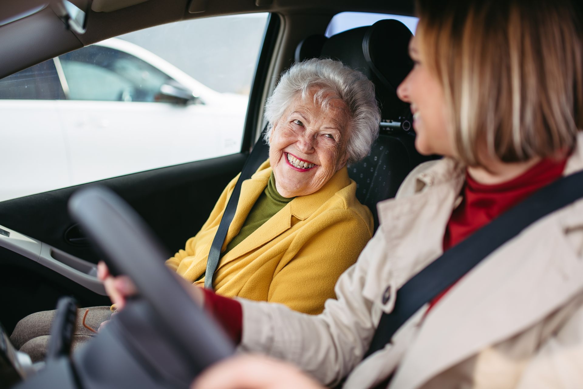 Elderly woman smiles from passenger seat as young woman drives.