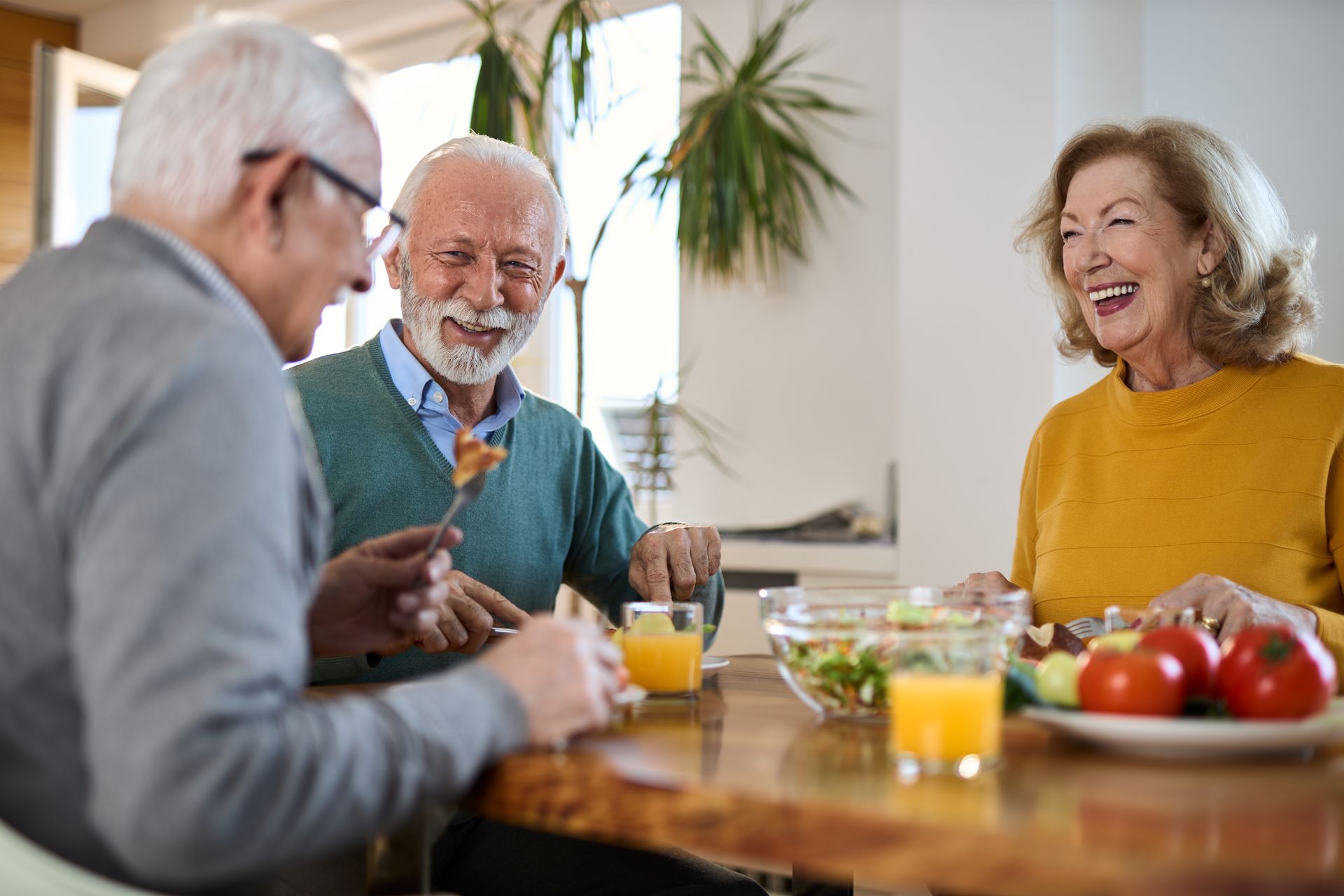 Three seniors laughing together at a table with food.