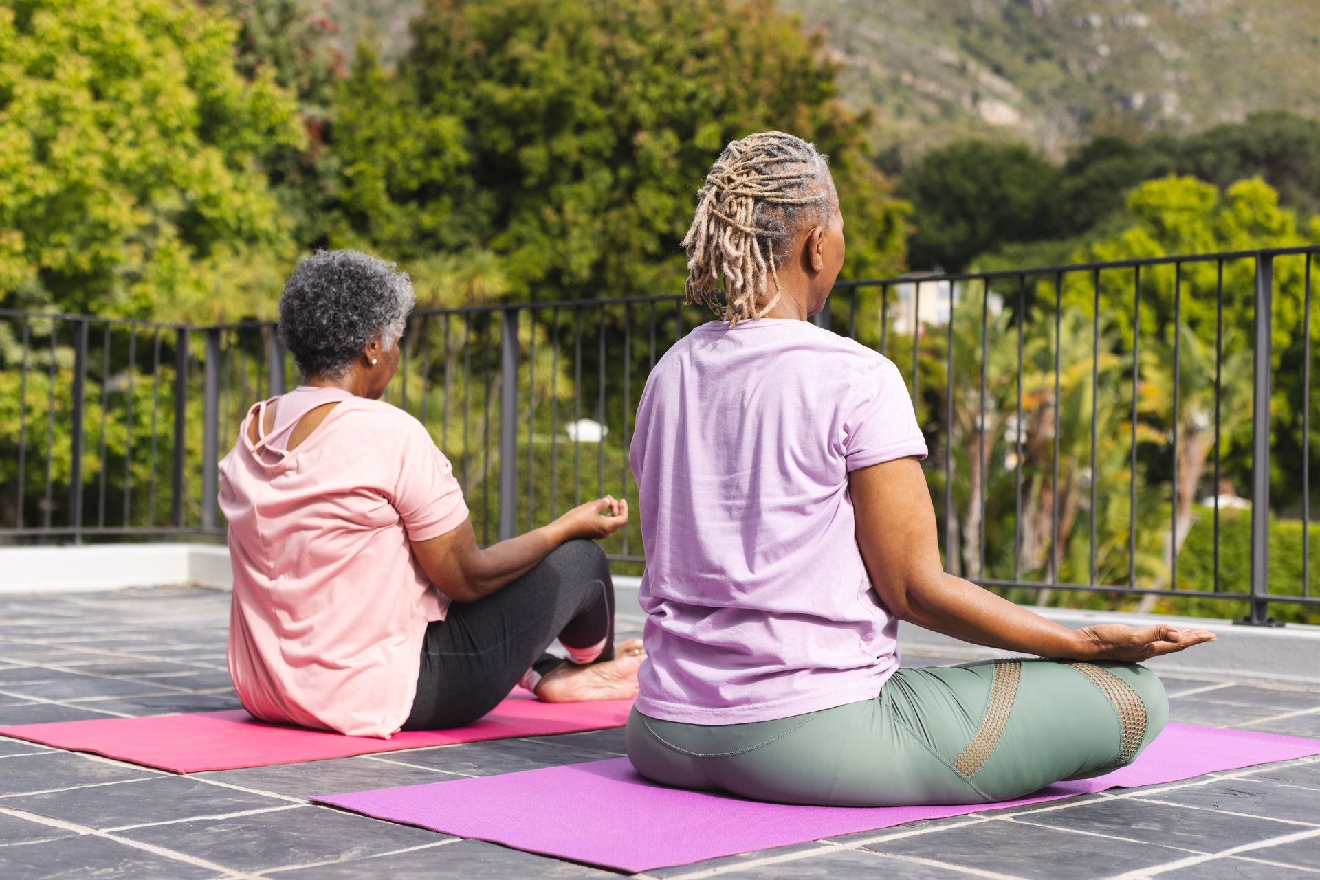 Two women doing yoga on mats outdoors with mountain view.