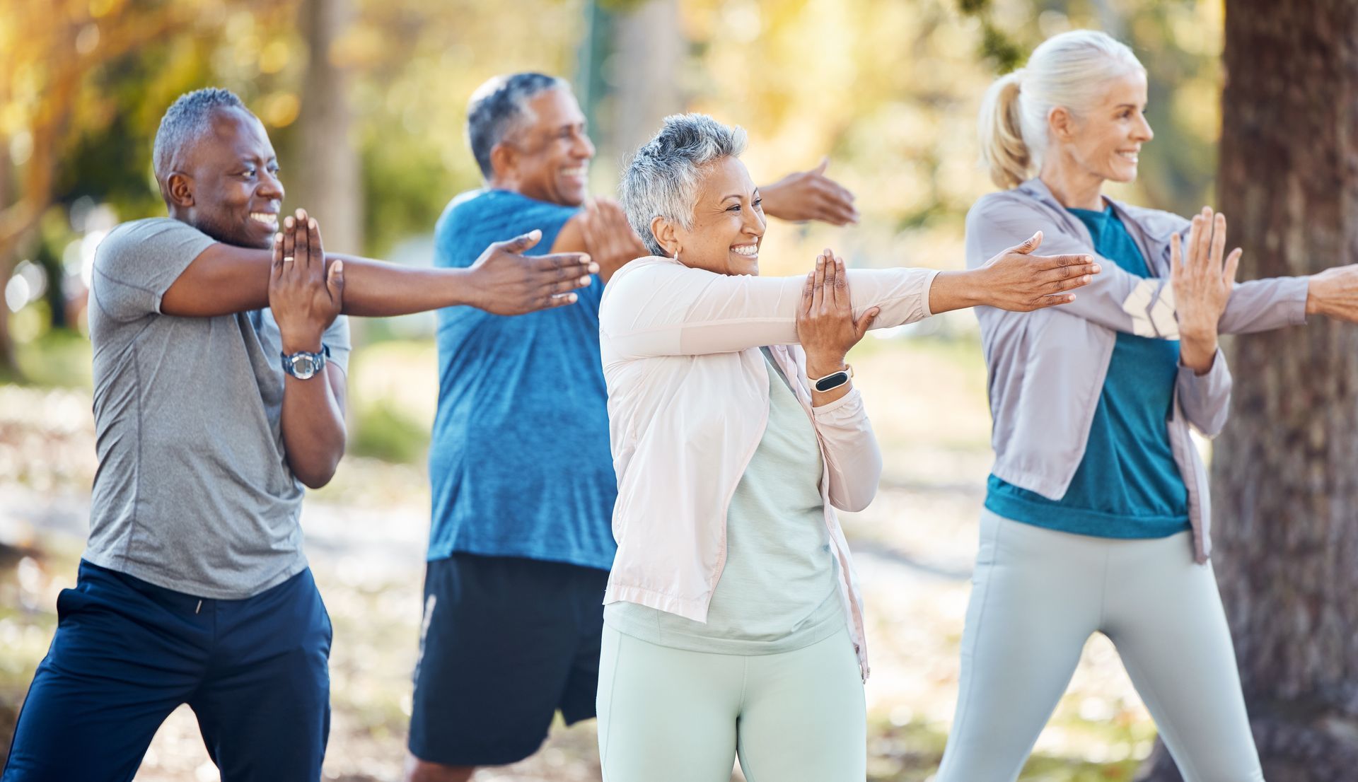 Four senior adults stretching outdoors, smiling.
