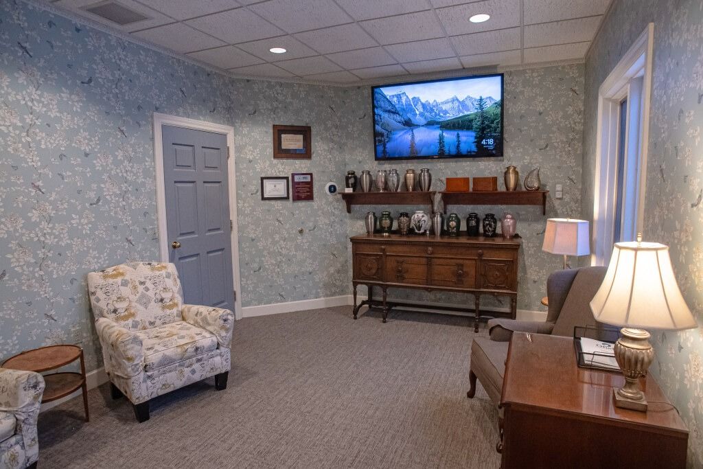 A comfortable room with floral chairs, a TV, and a wooden cabinet against a textured wall.