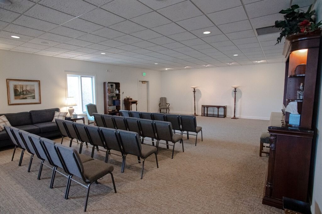 A sparsely furnished chapel with rows of chairs, a dark sofa, and a tall cabinet.