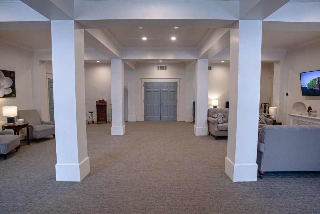 Interior of a light-filled room with columns and gray carpet. Two blue double doors are centered at the back.