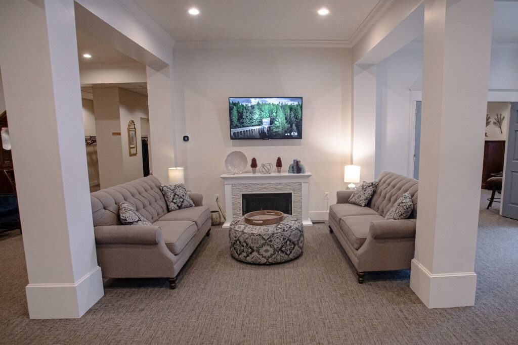 Living room with two sofas facing a fireplace, TV on the wall, and decorative ottoman.