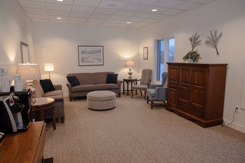 Cozy living room with beige carpet, sofas, chairs, lamps, cabinet, artwork, and an ottoman.