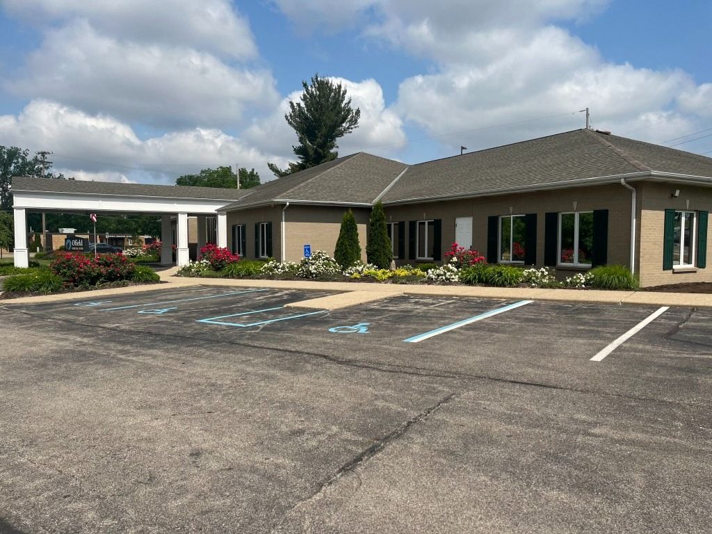 Tan building with covered entrance, parking spaces, landscaping and blue sky.
