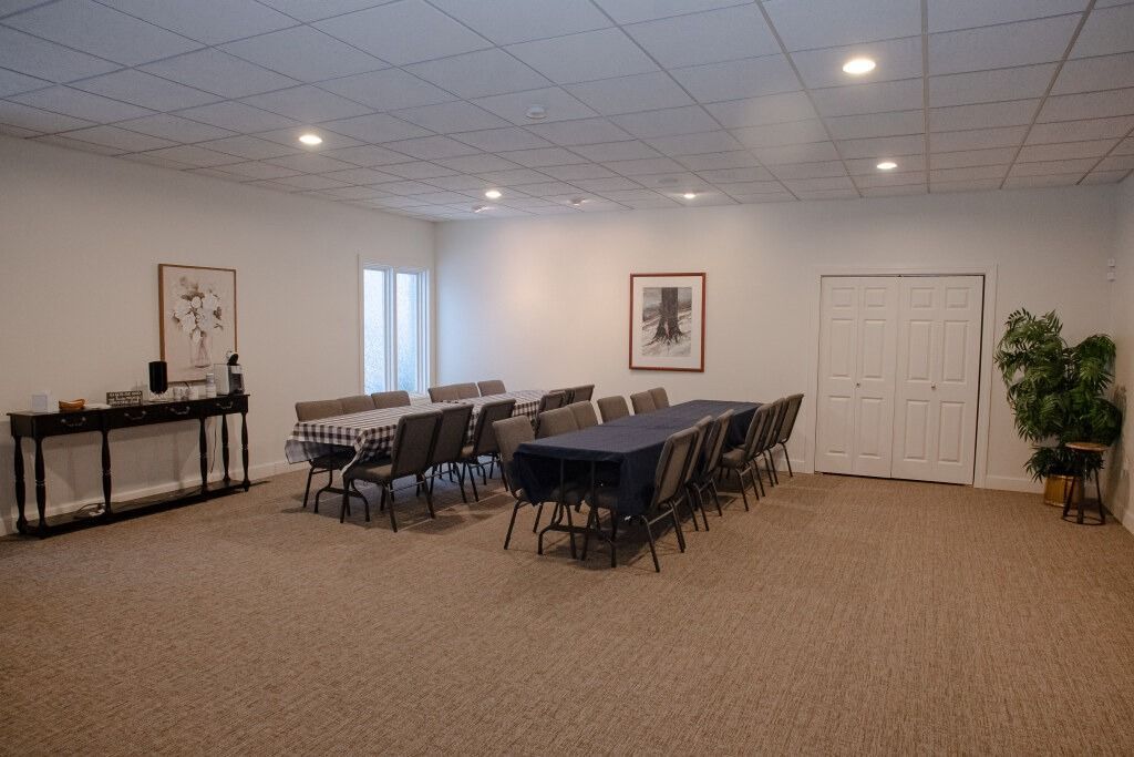 Meeting room with tables, chairs, and a plant. Neutral tones with recessed lighting.