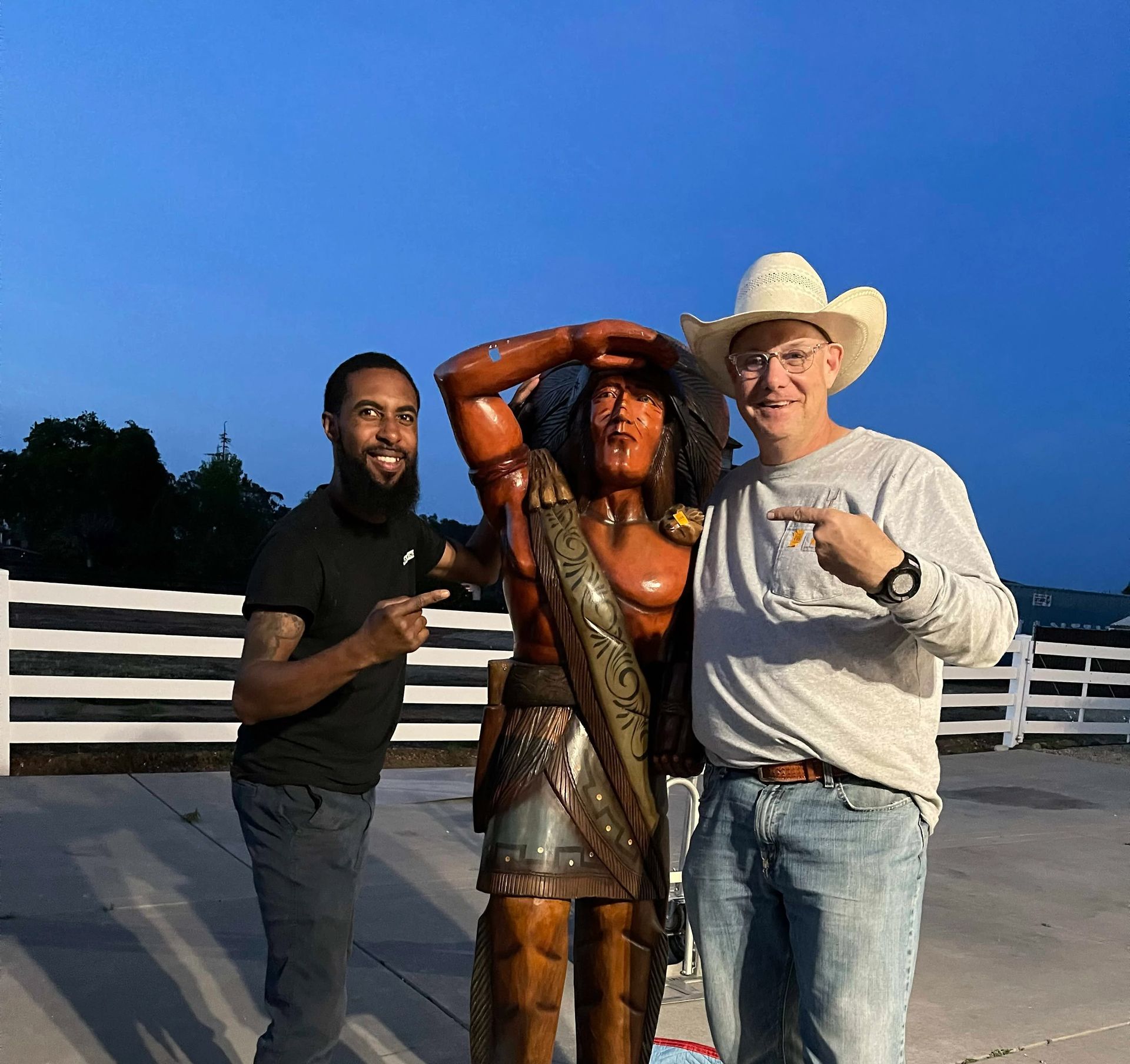 A man in a cowboy hat is pointing at a statue