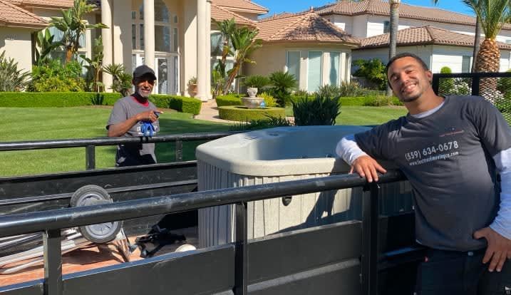 Two men are standing next to a trailer with a hot tub in it.