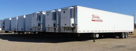 Several white refrigerated semi-truck trailers parked outdoors on a clear, sunny day. Some units have visible cooling systems.