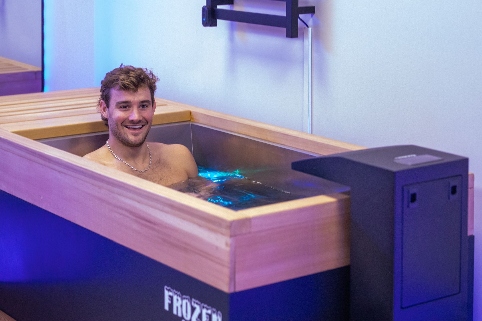 Woman in a black swimsuit relaxing in a hot tub, eyes closed, arms resting, steam visible, wooden backdrop.