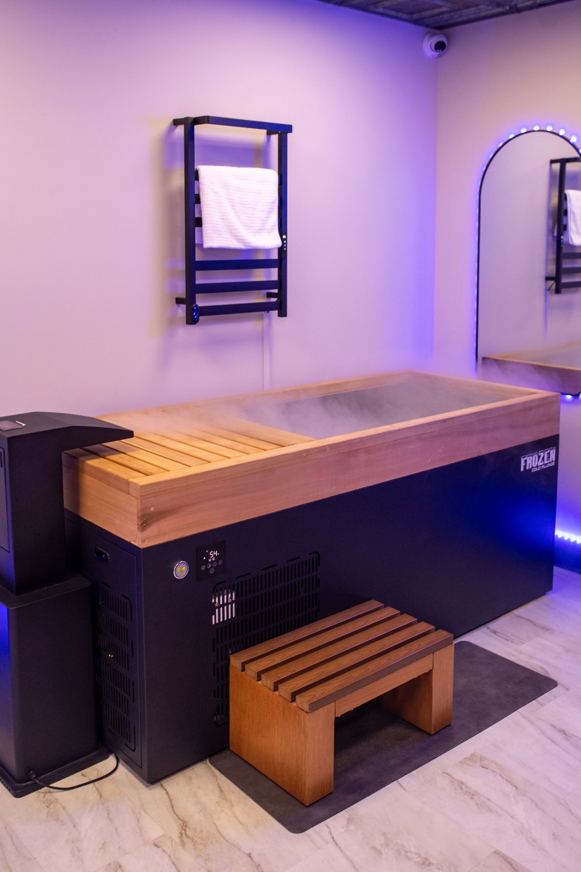 Woman in a black swimsuit relaxing in a hot tub, eyes closed, arms resting, steam visible, wooden backdrop.