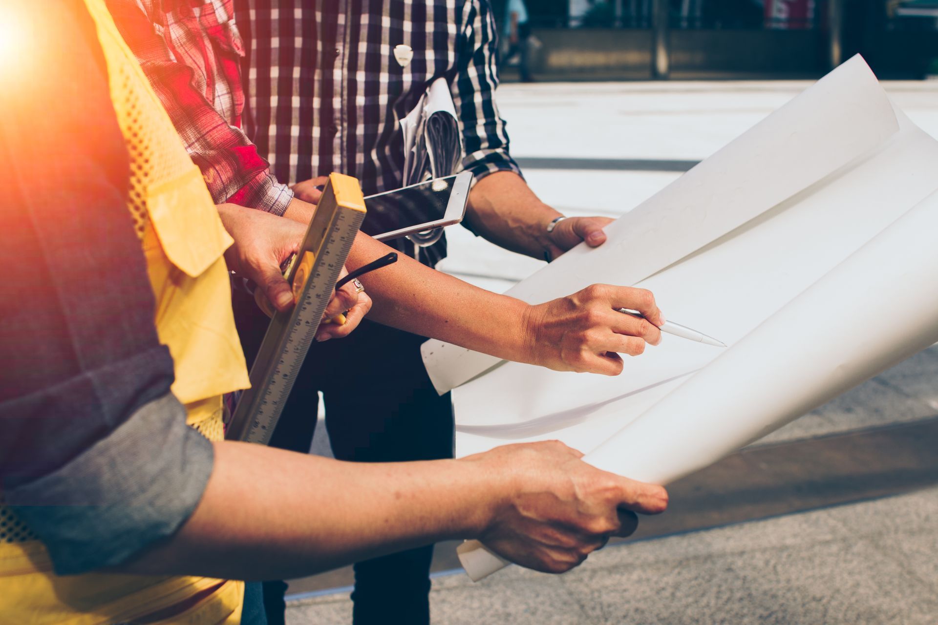 People reviewing architectural blueprints together outdoors in bright sunlight