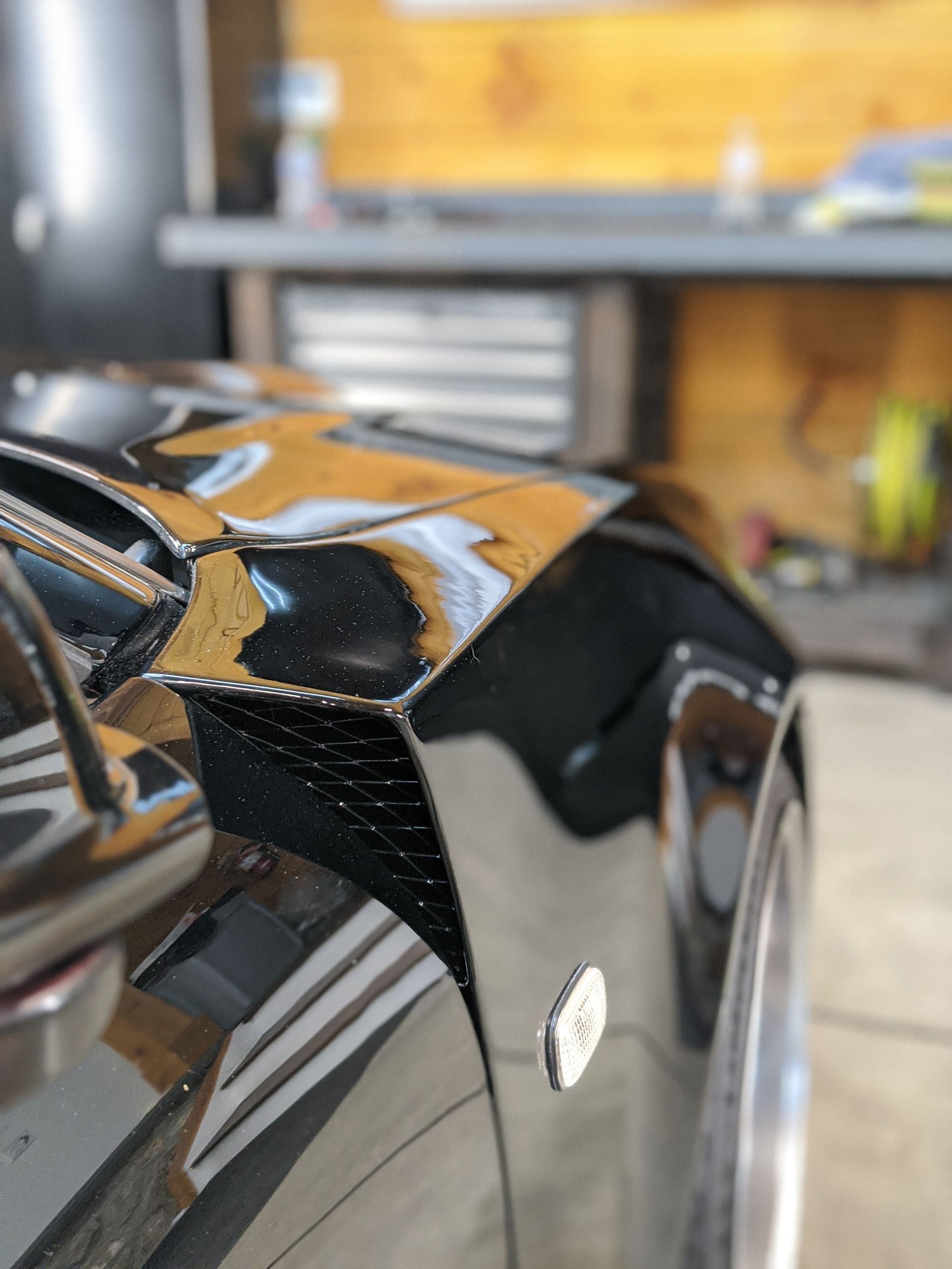Close-up of a glossy black car fender in a garage, with reflections and a white wheel visible.