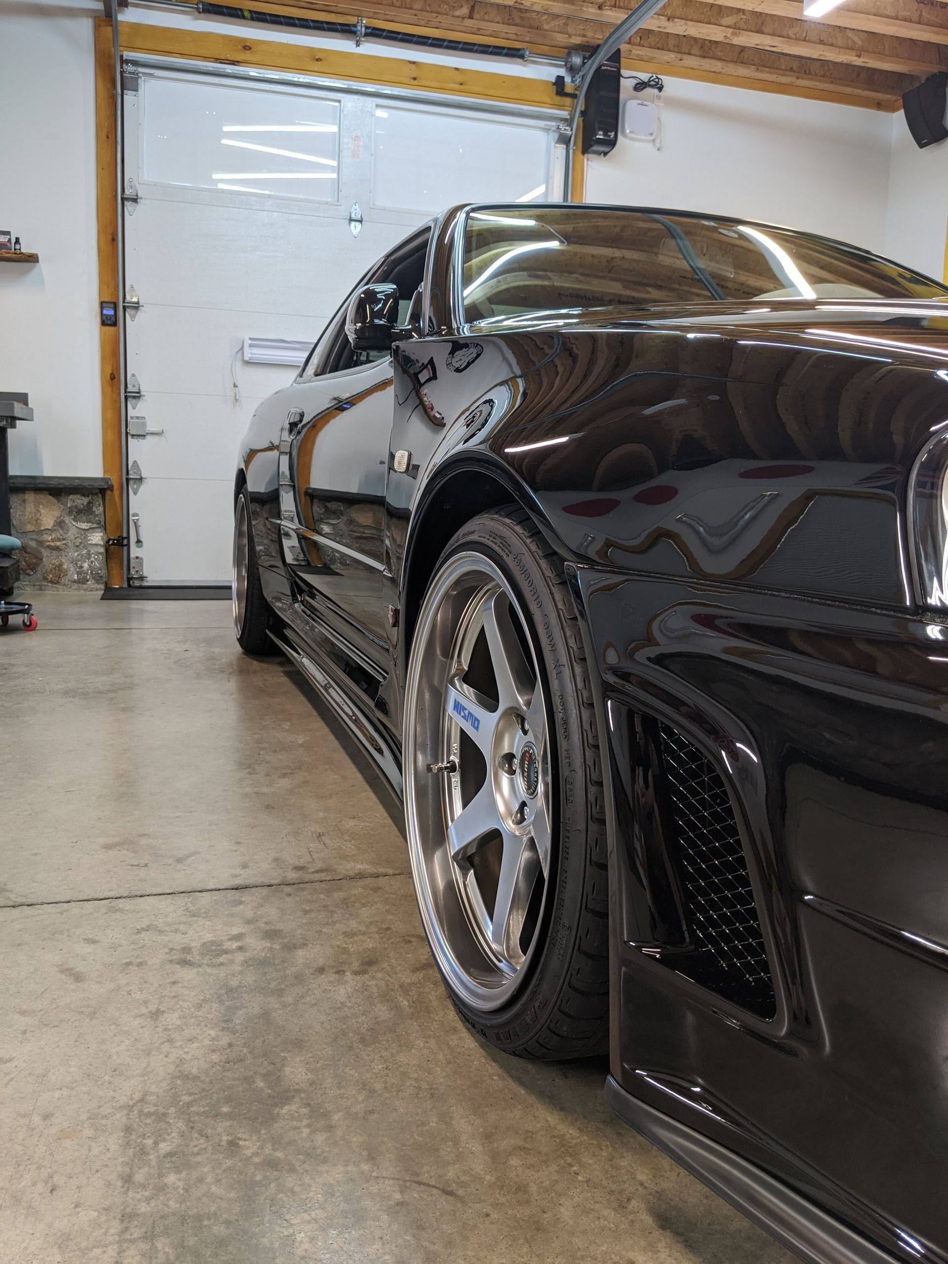 Black sports car in a garage, seen from the side with shiny chrome wheels.