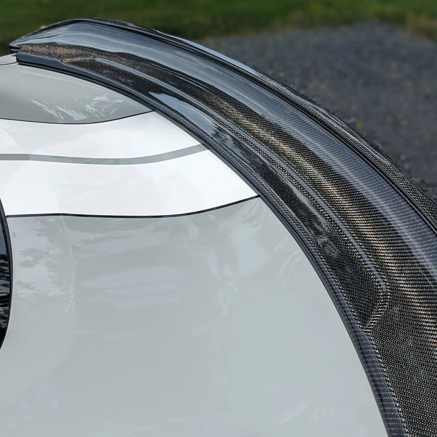 Close-up of a carbon-fiber car spoiler on a white vehicle.