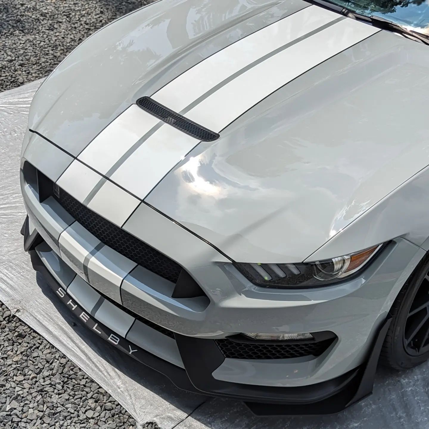 Gray sports car with black racing stripes, viewed from the front on a road.