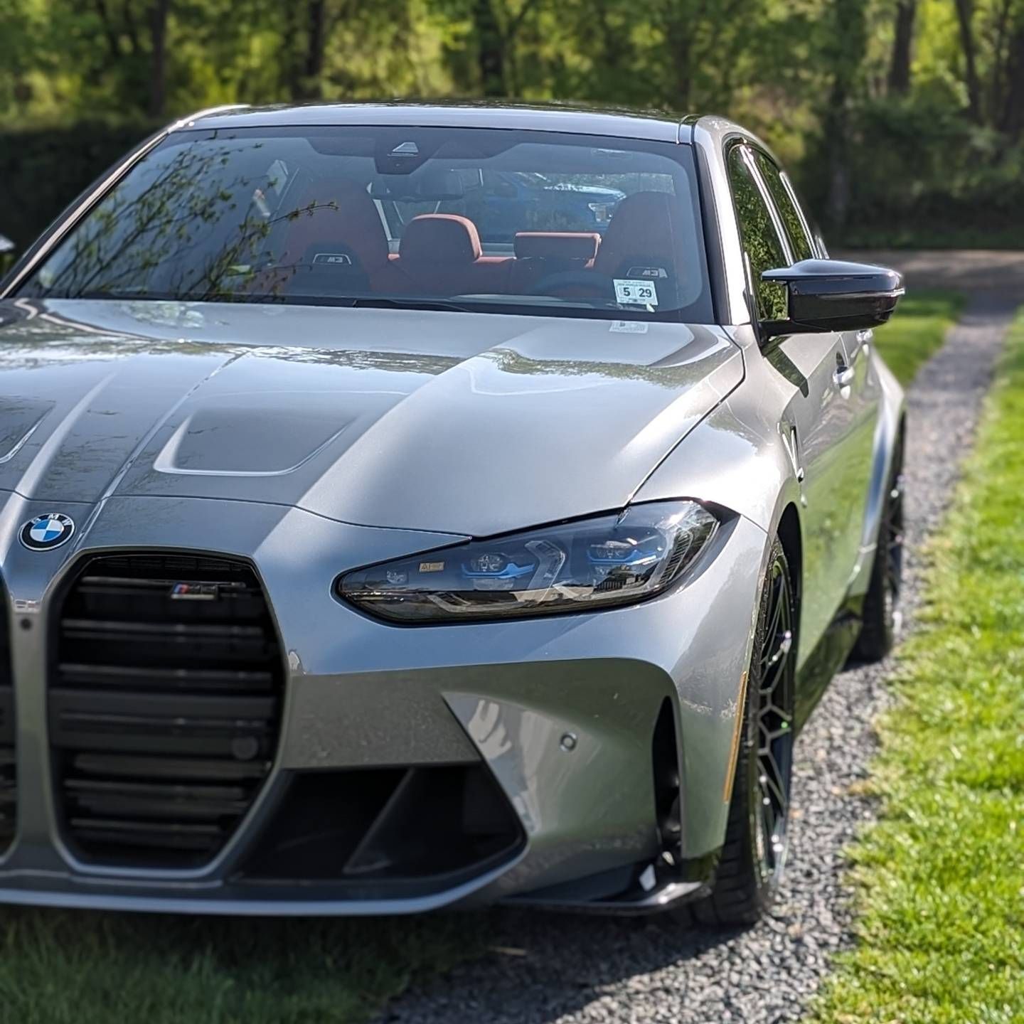 Silver BMW sports sedan parked on a gravel roadside beside green trees