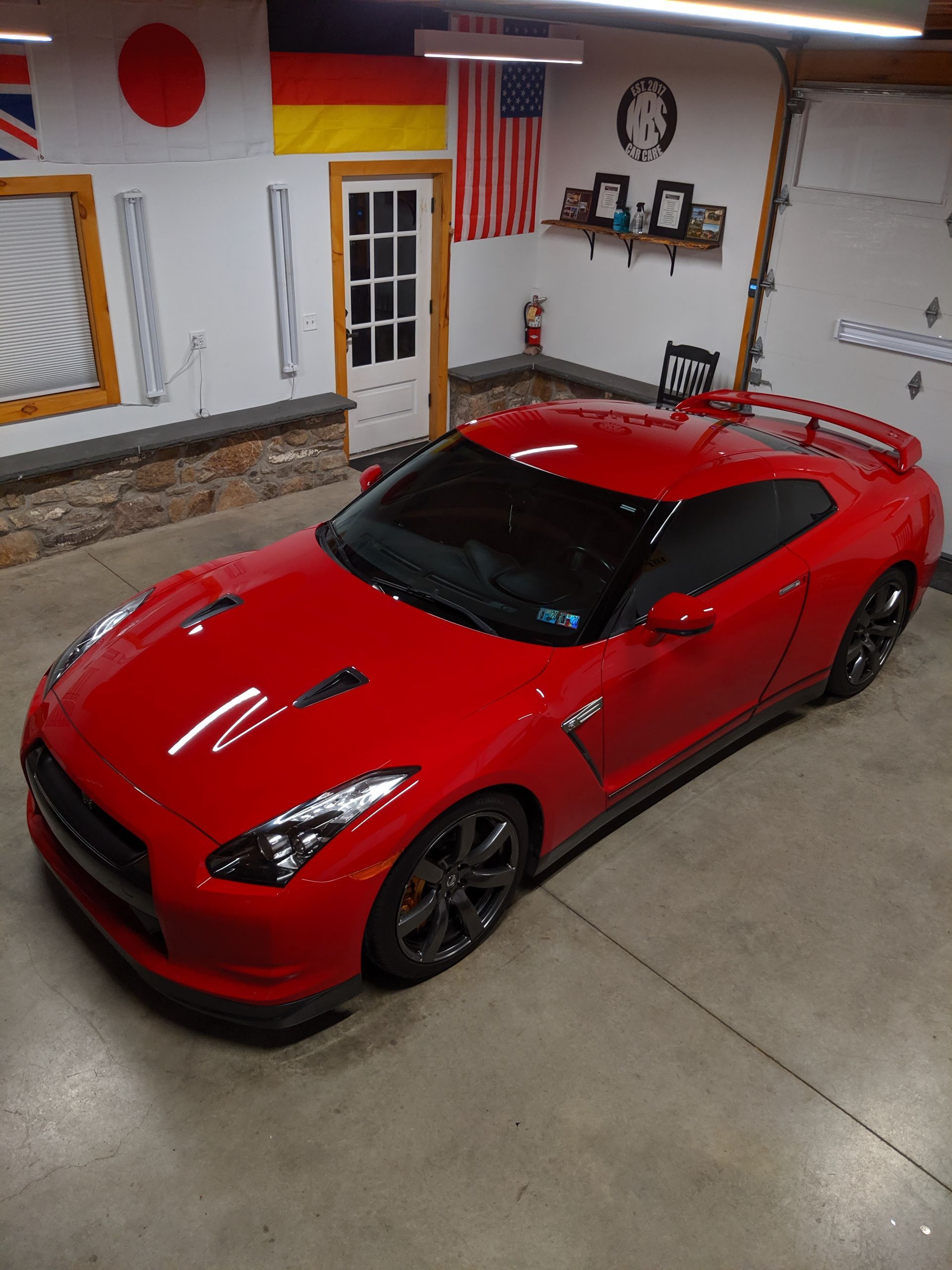 Red sports car parked in a garage with an American flag and tools on the wall.