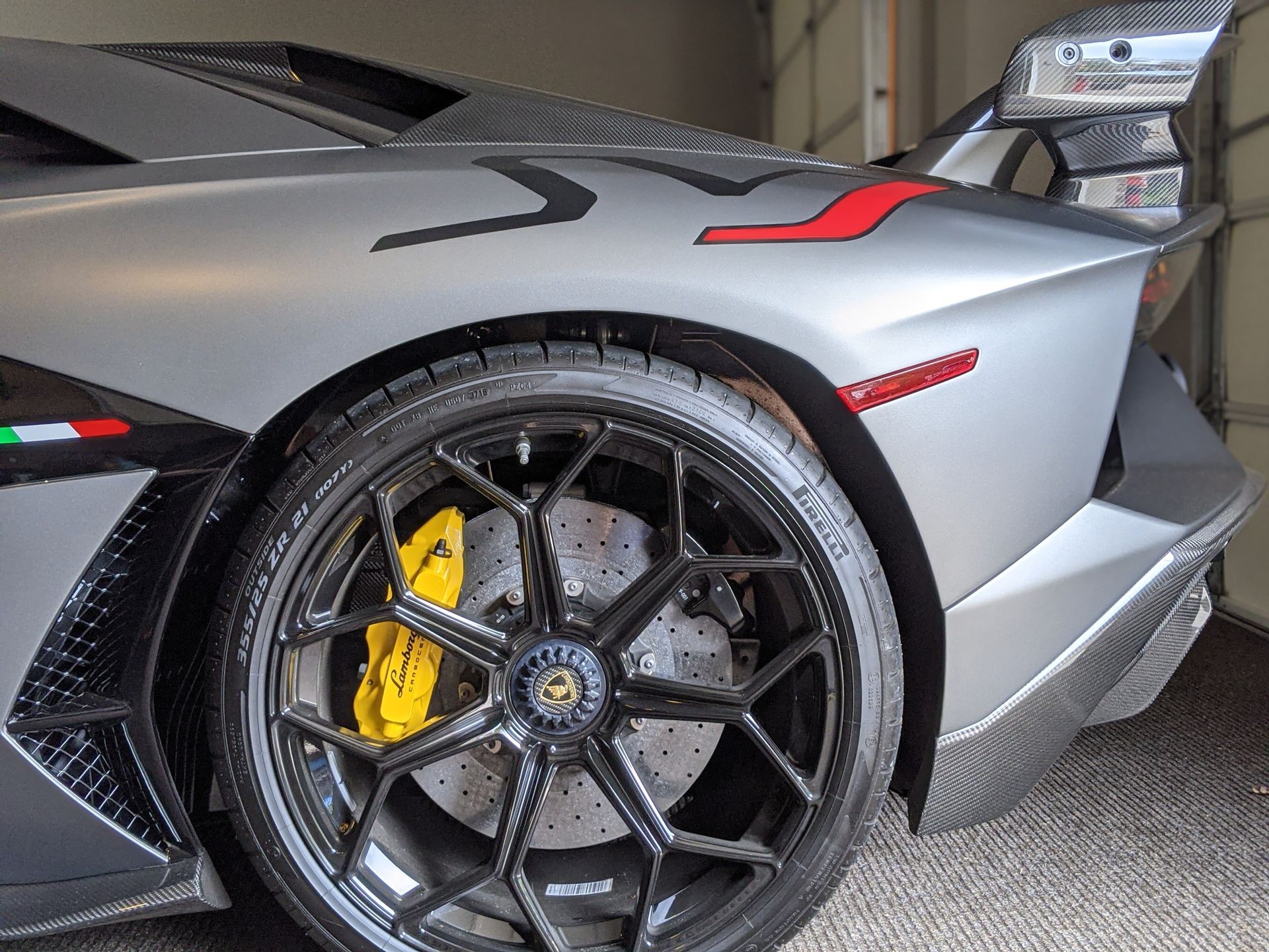 Close-up of a gray Lamborghini’s rear wheel, yellow brake caliper, and red accents in a garage
