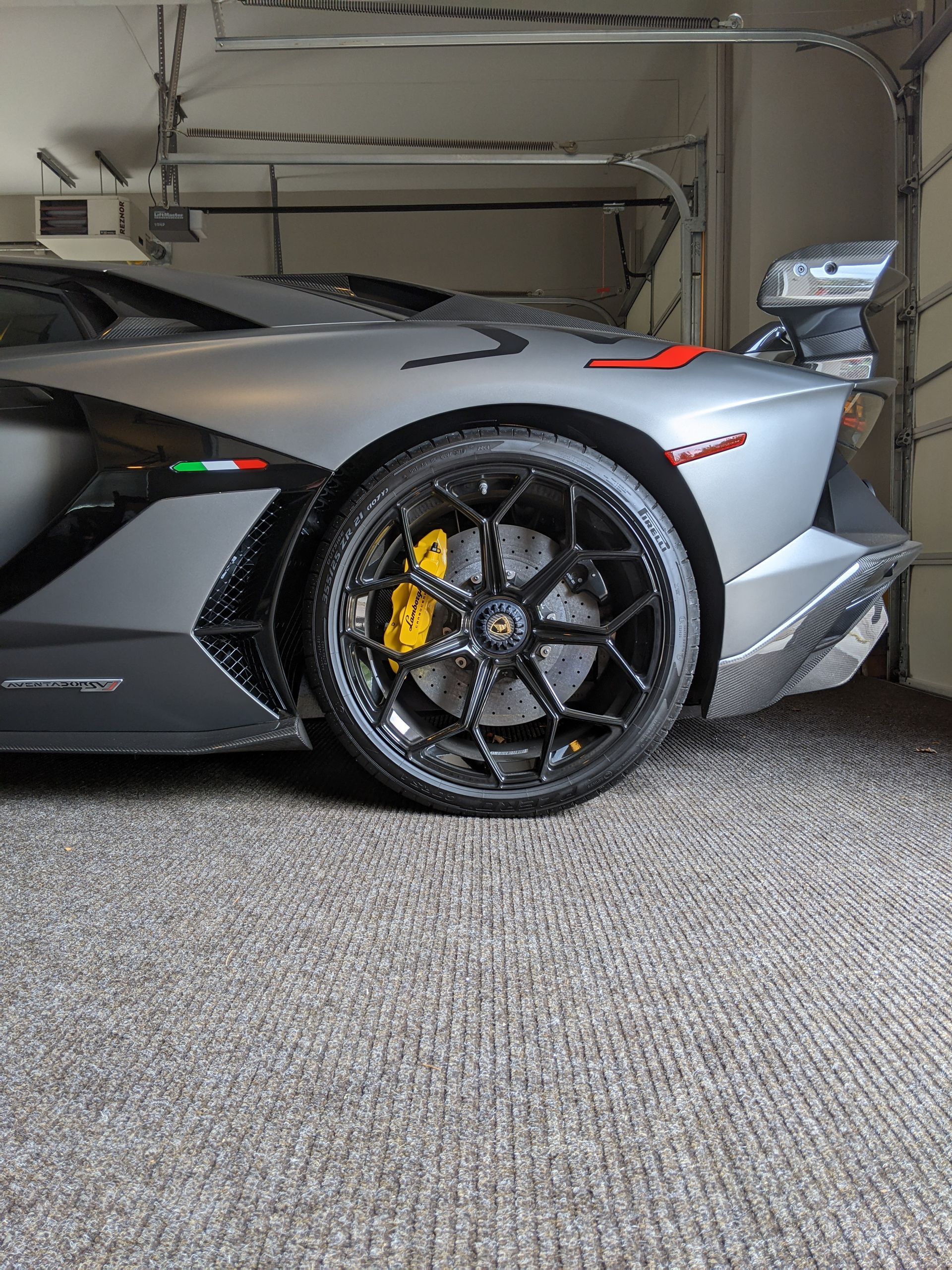 Gray Lamborghini with black wheels parked in a garage, rear side view