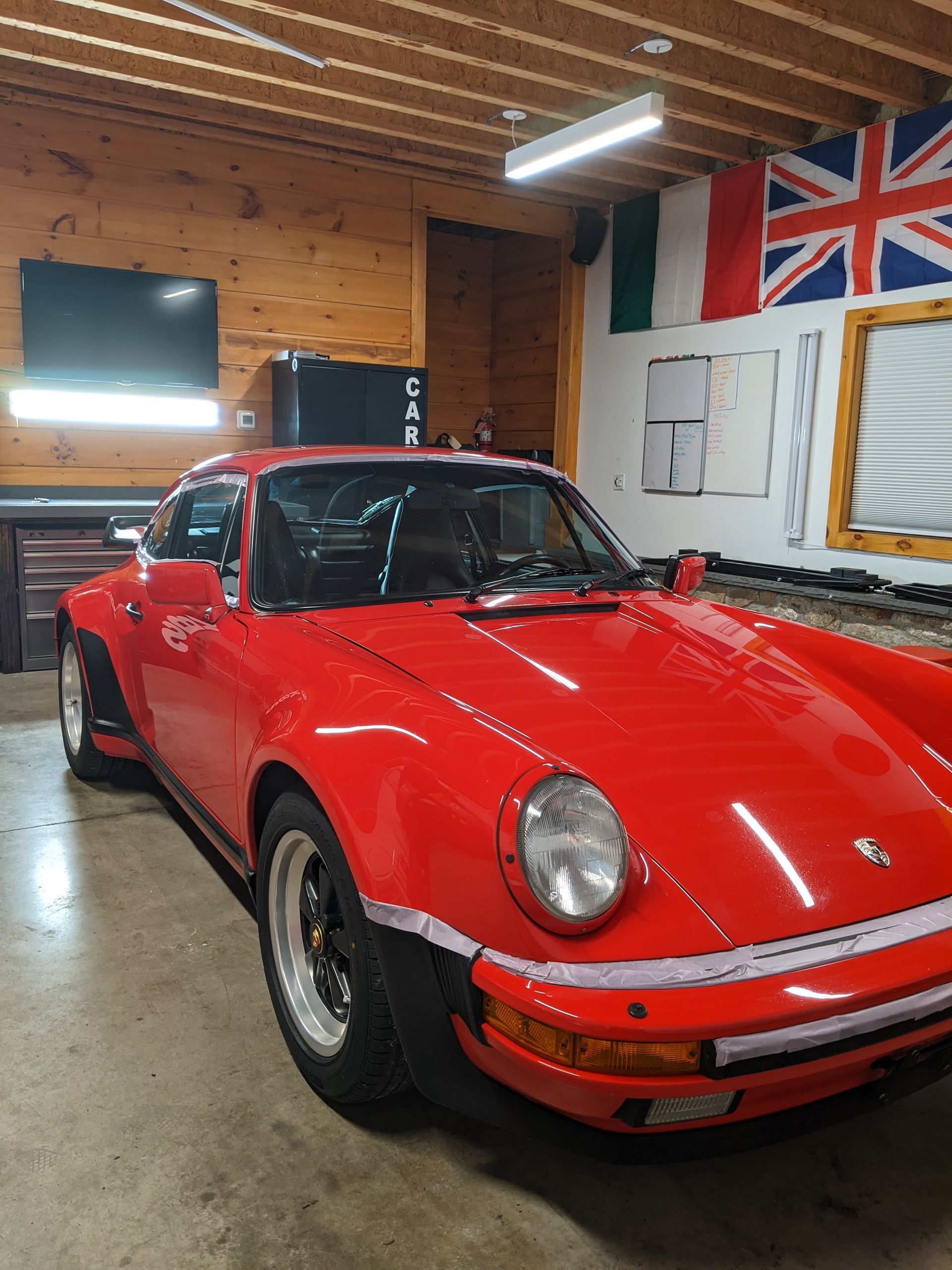 Red classic Porsche in a wood-paneled garage with flags on the wall.