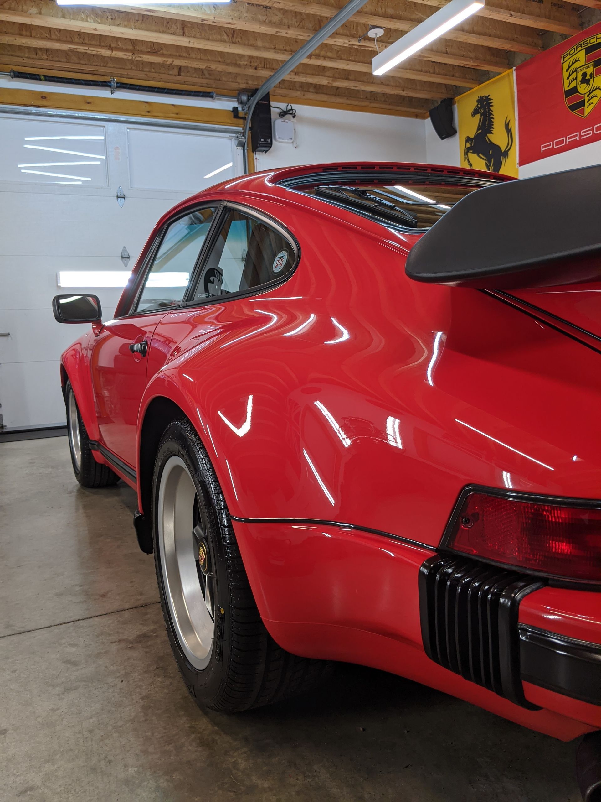 Red sports car in a garage, rear three-quarter view, with a large black rear wing.