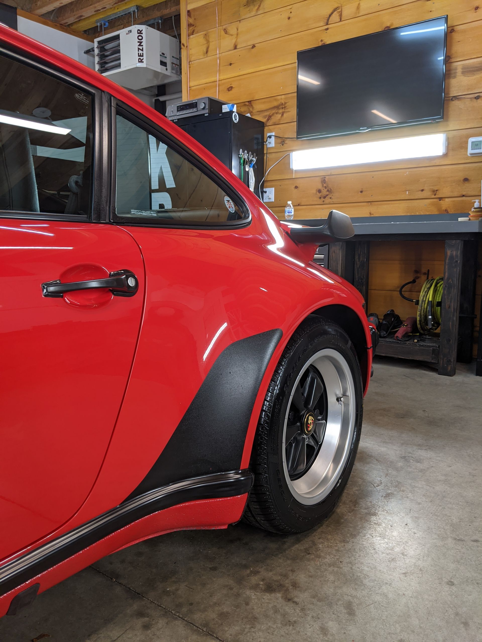 Red vintage car parked in a garage with wood walls and a wall-mounted TV.