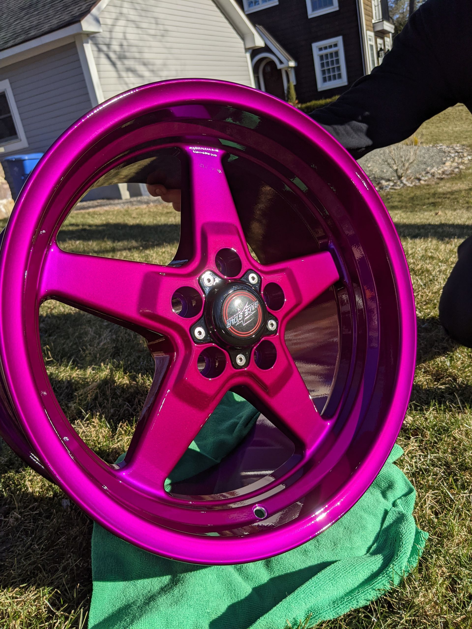 Magenta five-spoke car wheel rim leaning on grass outdoors