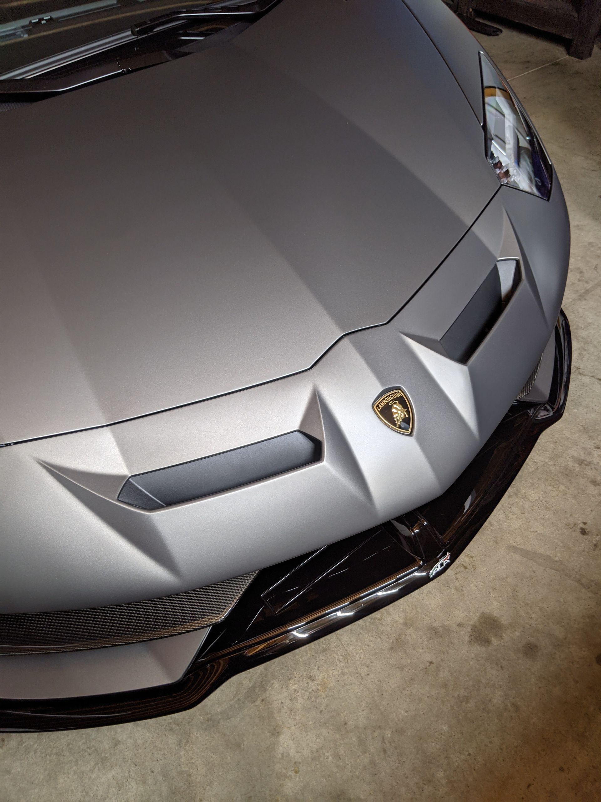 Silver Lamborghini front end parked in a garage, with a black carbon-fiber splitter visible.