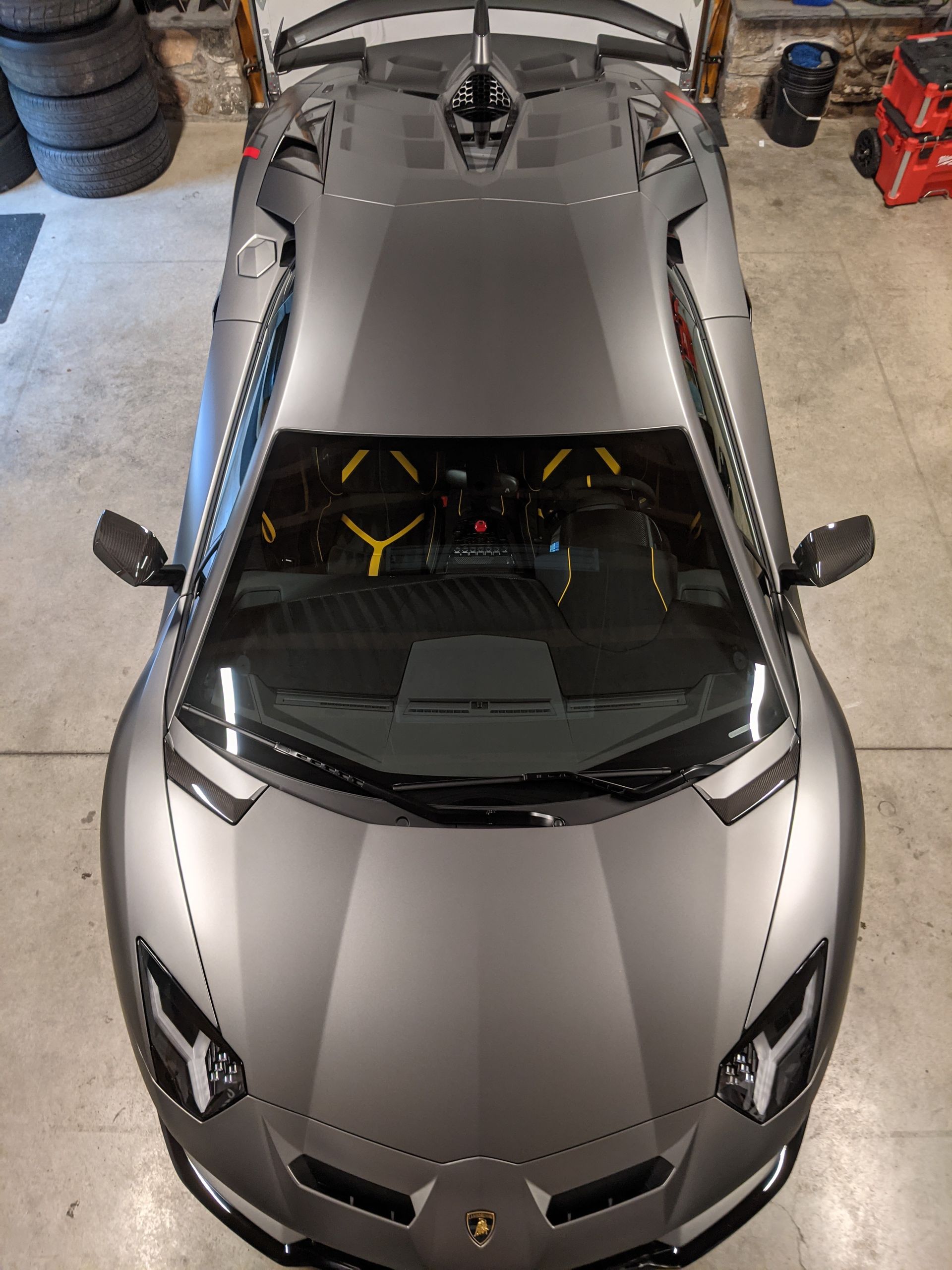 Silver Ferrari sports car viewed from above in a garage, showing a black windshield and hood vents