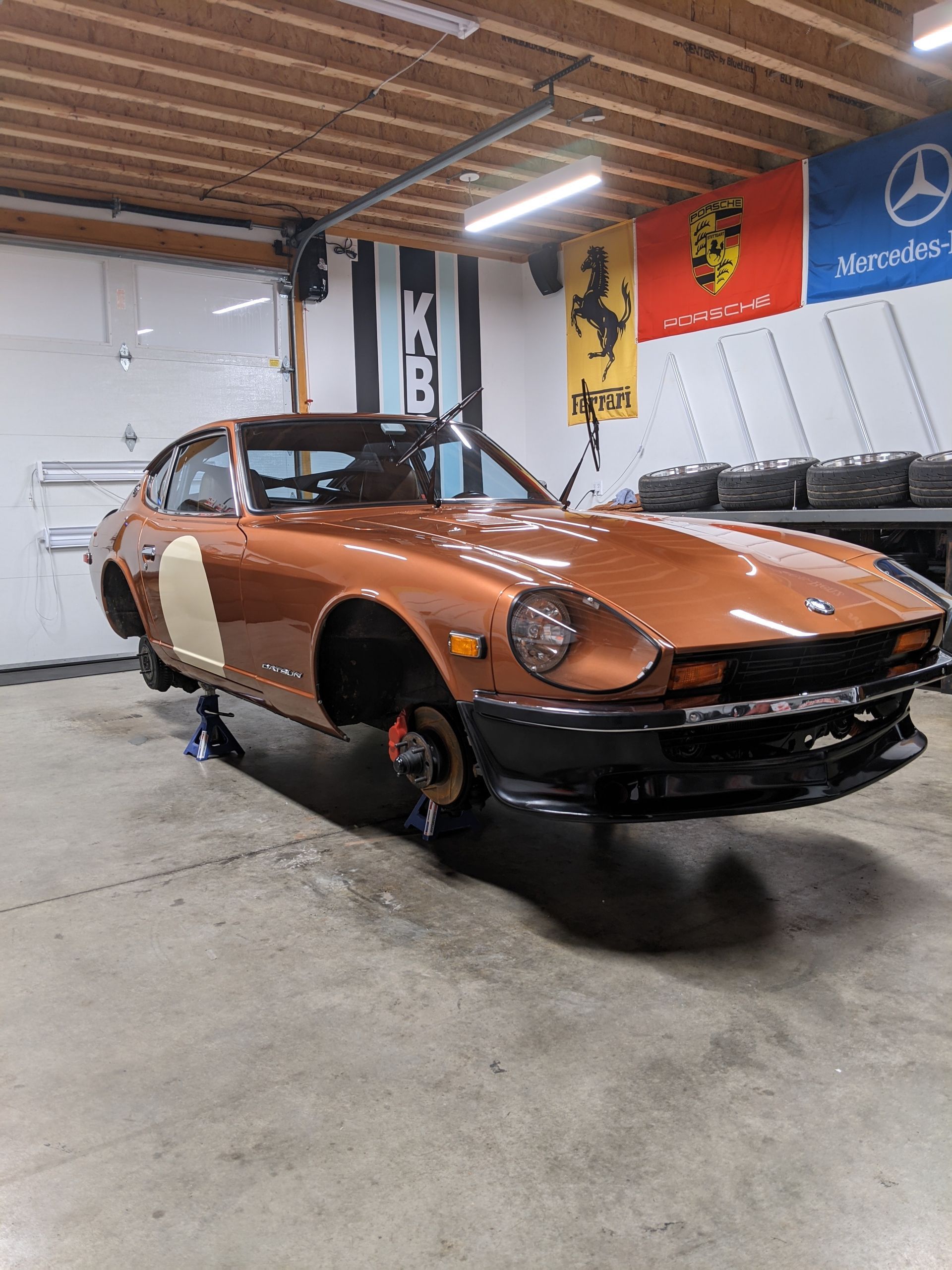 Orange classic sports car on jacks in a garage, with a black front end and exposed wheels.