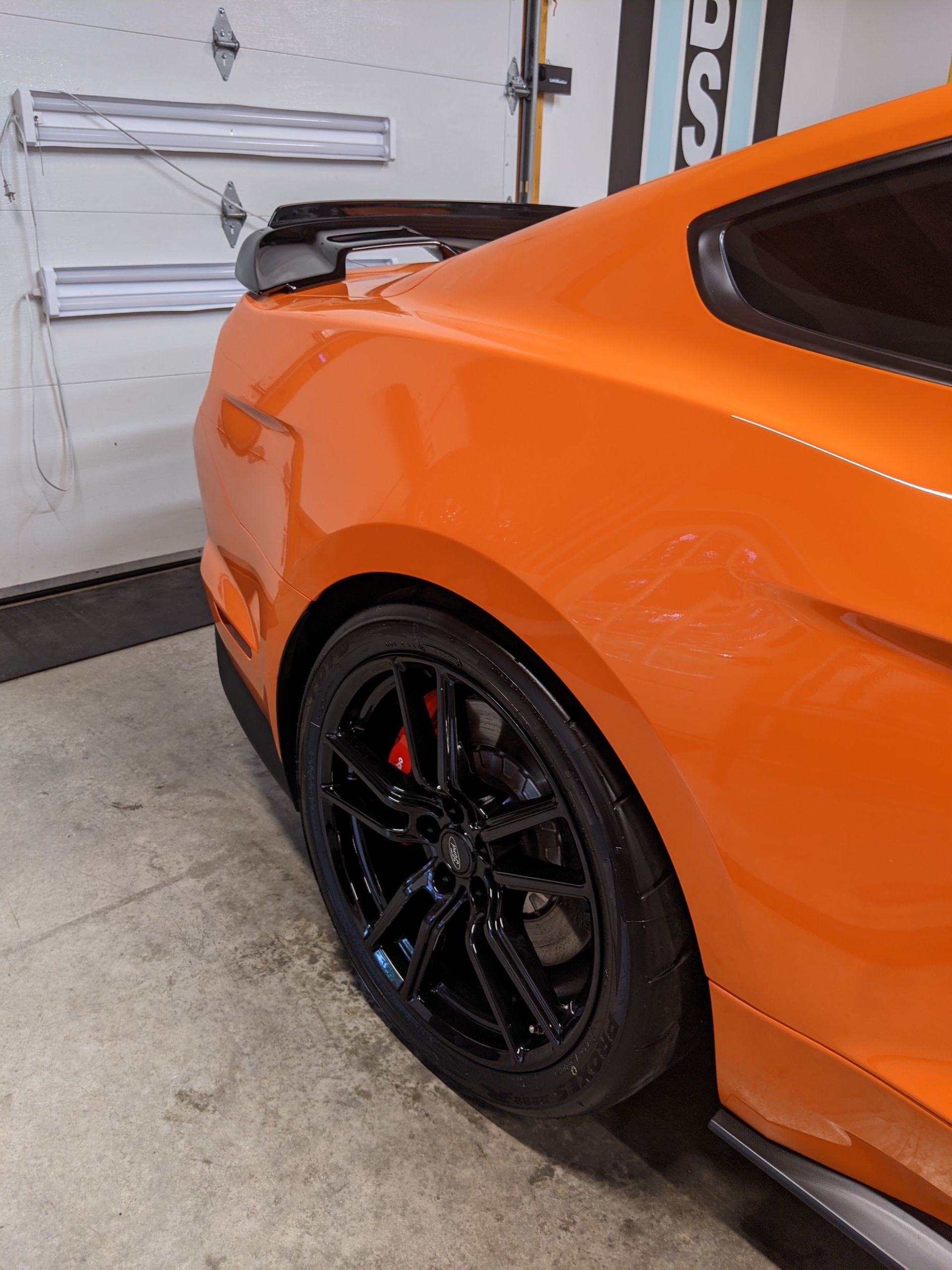 Orange sports car rear quarter with black wheel in a garage