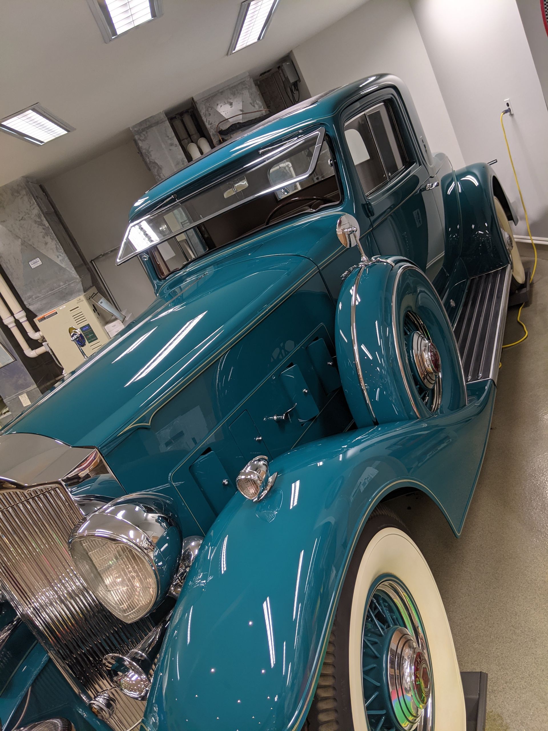 Teal vintage car with whitewall tires displayed indoors under bright lights