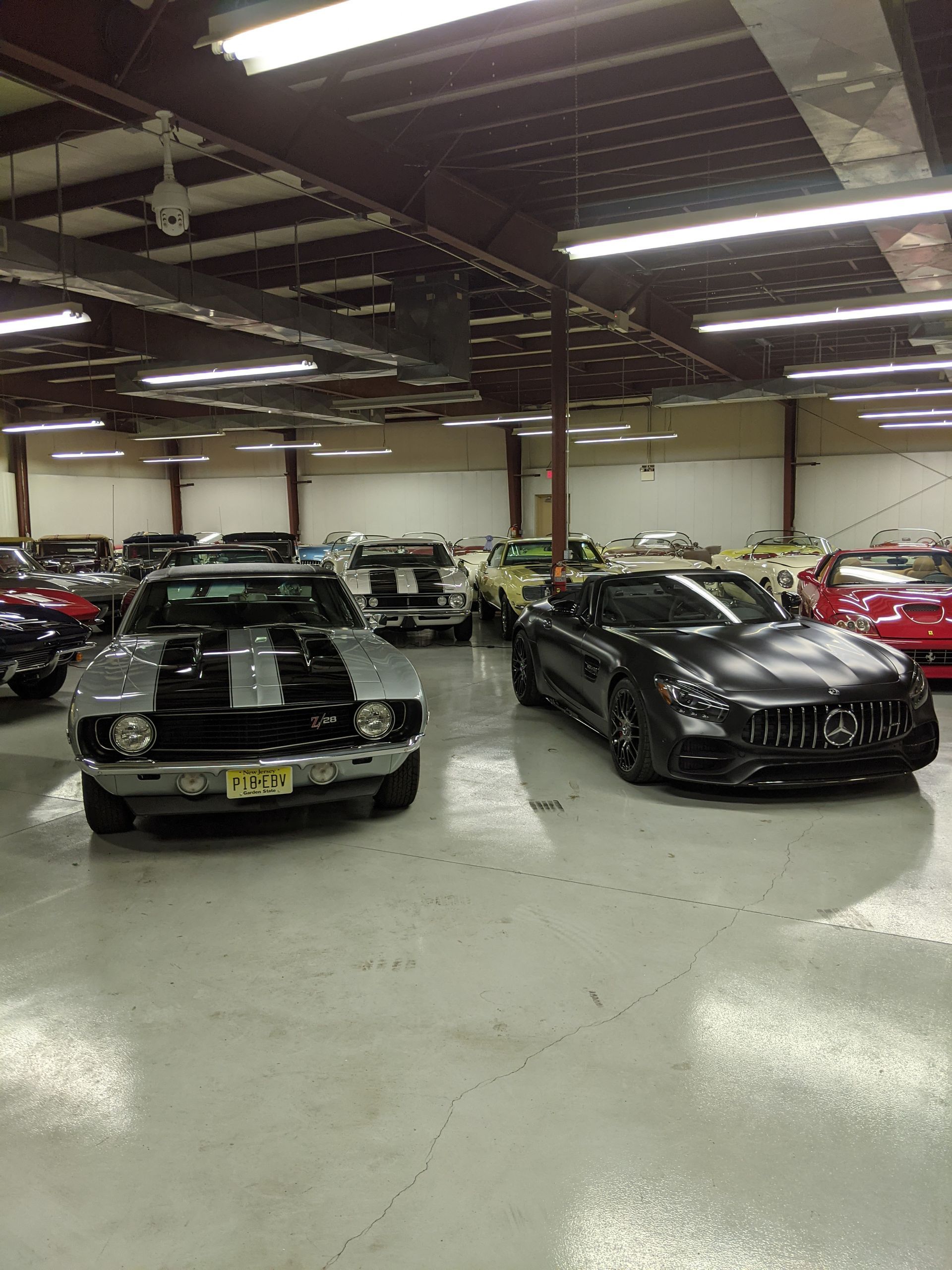 Rows of classic cars parked in a large indoor garage with bright overhead lights.