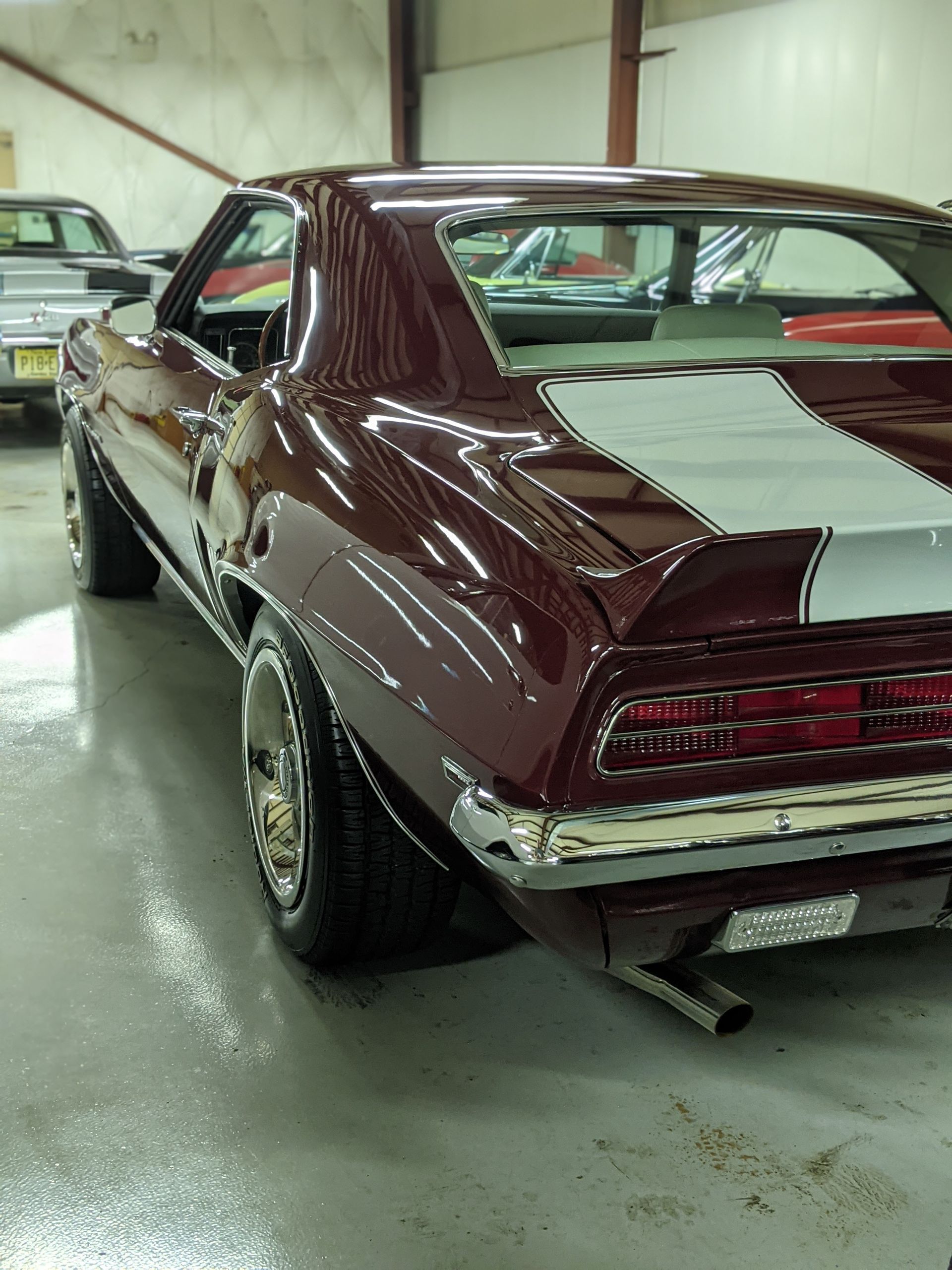 Maroon classic muscle car parked indoors in a garage, rear three-quarter view