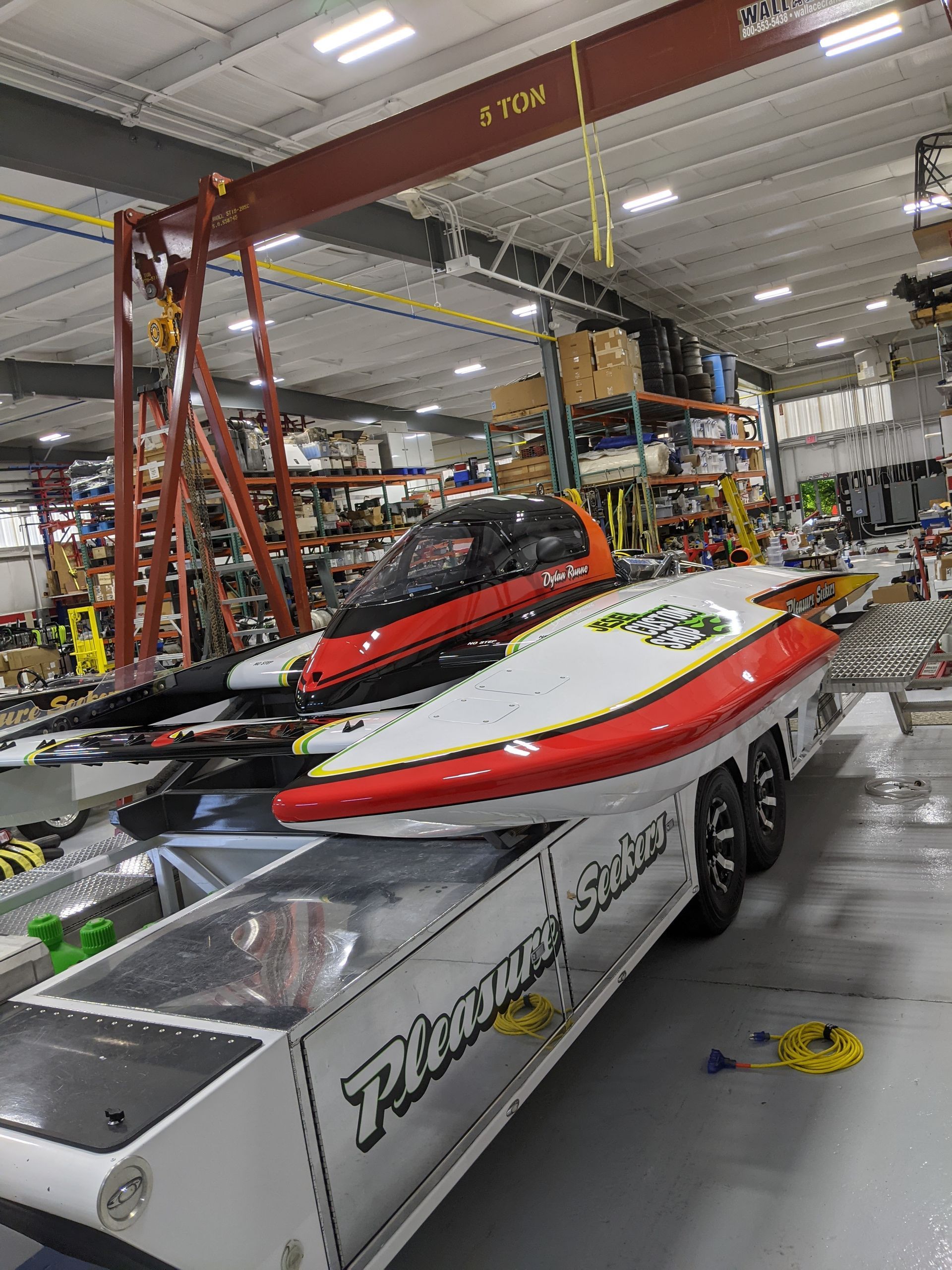 Jet skis on a trailer inside a warehouse, with red and white boats in the foreground.