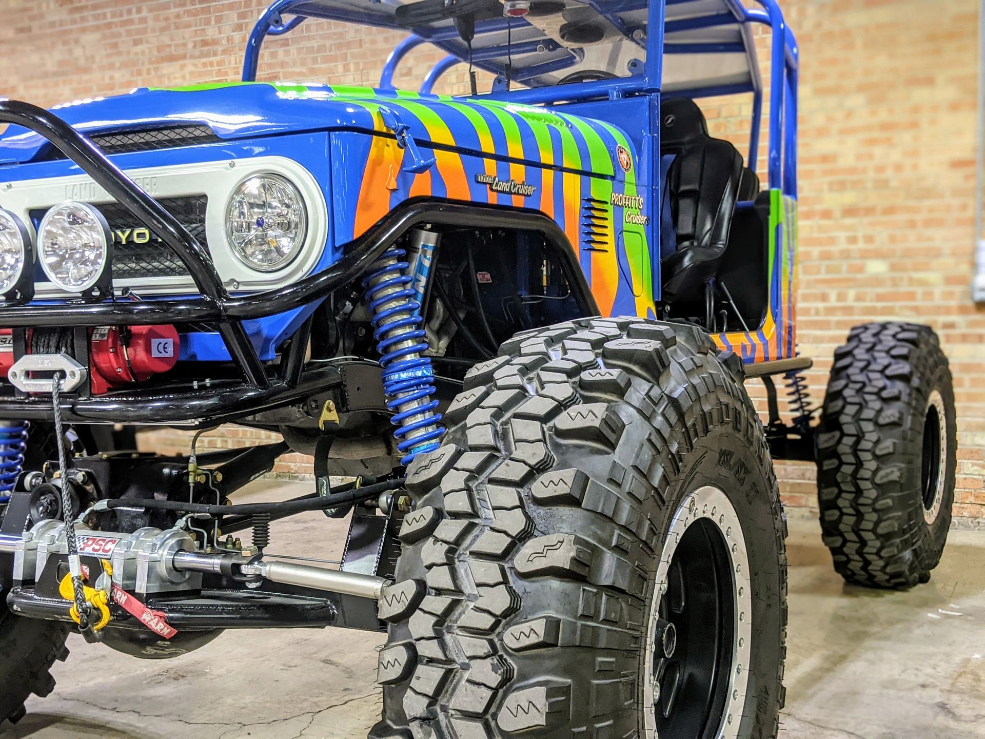 Blue off-road buggy with oversized tires and roll cage parked on concrete floor